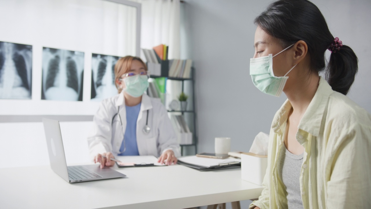 自信的亚洲女医生戴着防护口罩，年轻的病人女孩看着镜头微笑着在健康诊所或医院的办公桌上进行医疗咨询。视频素材