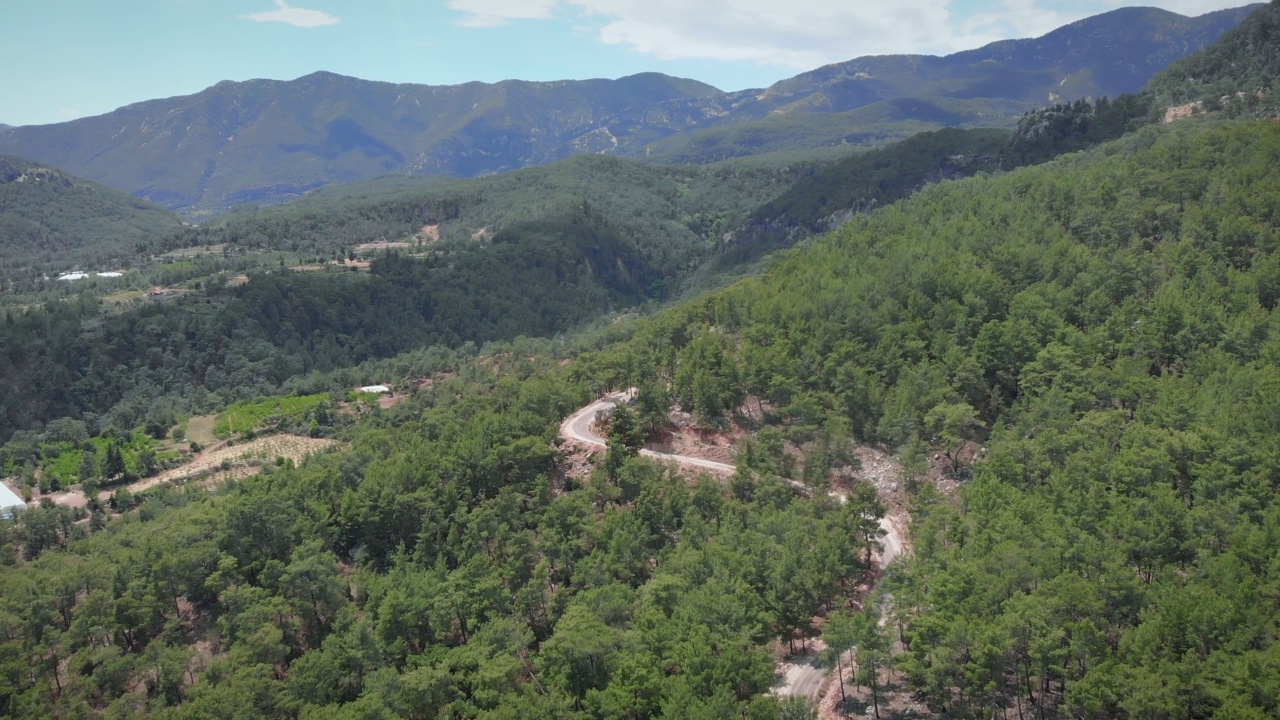 蜿蜒狭窄的山路在绿树成荫的森林里。空旷的汽车道路之间的山丘陵。阳光明媚的夏日，美丽的山景。从鸟瞰青山的山峰。视频素材