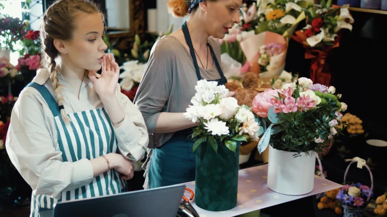 忙碌的女花匠在花店工作。一个成熟的女人和一个年轻的女孩正在考虑在一家花店订购视频素材