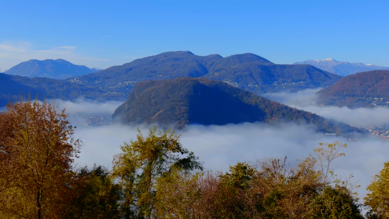 秋天阳光明媚的日子里，意大利边境的卢加诺高山湖与云海和山脉的全景视频素材