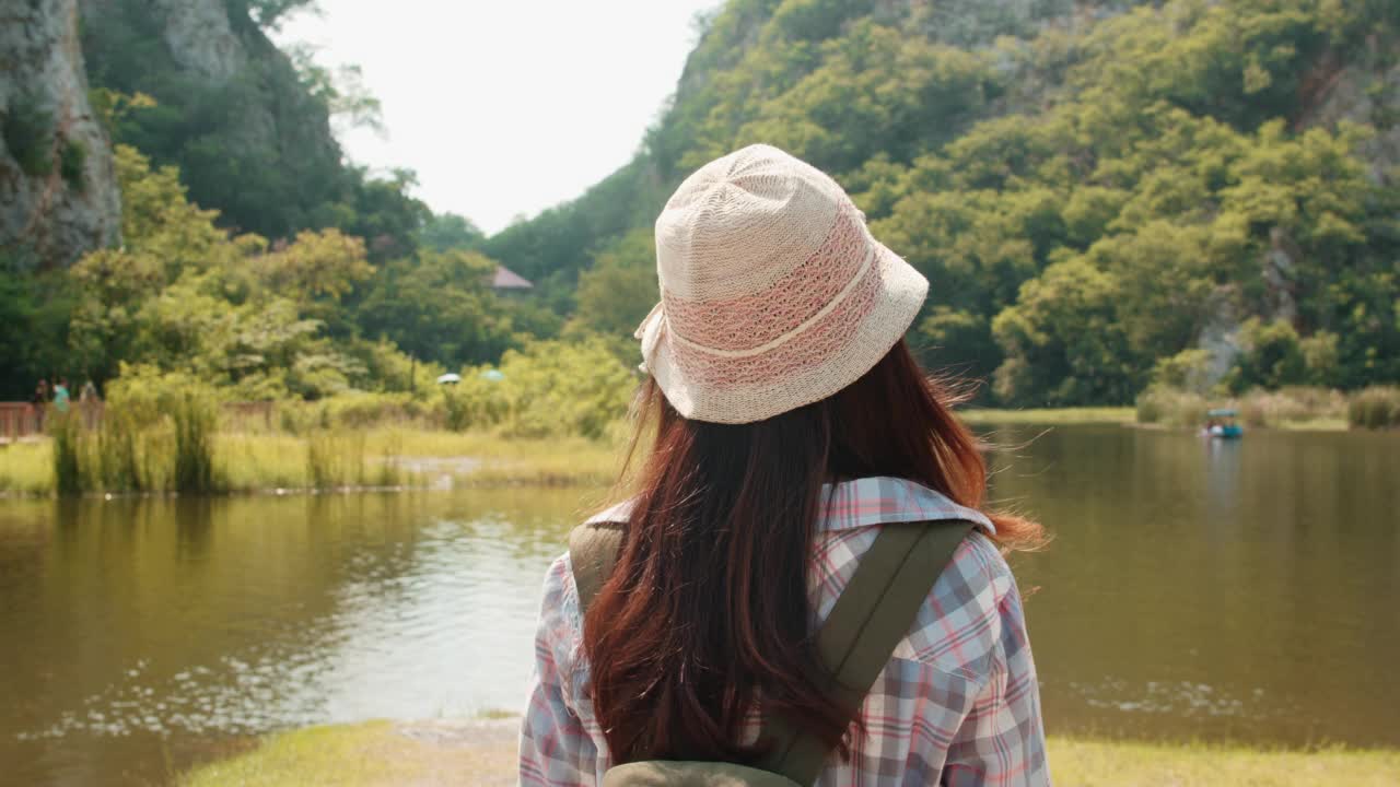 开朗的年轻旅行者与背包在山湖散步的亚洲女士。视频素材