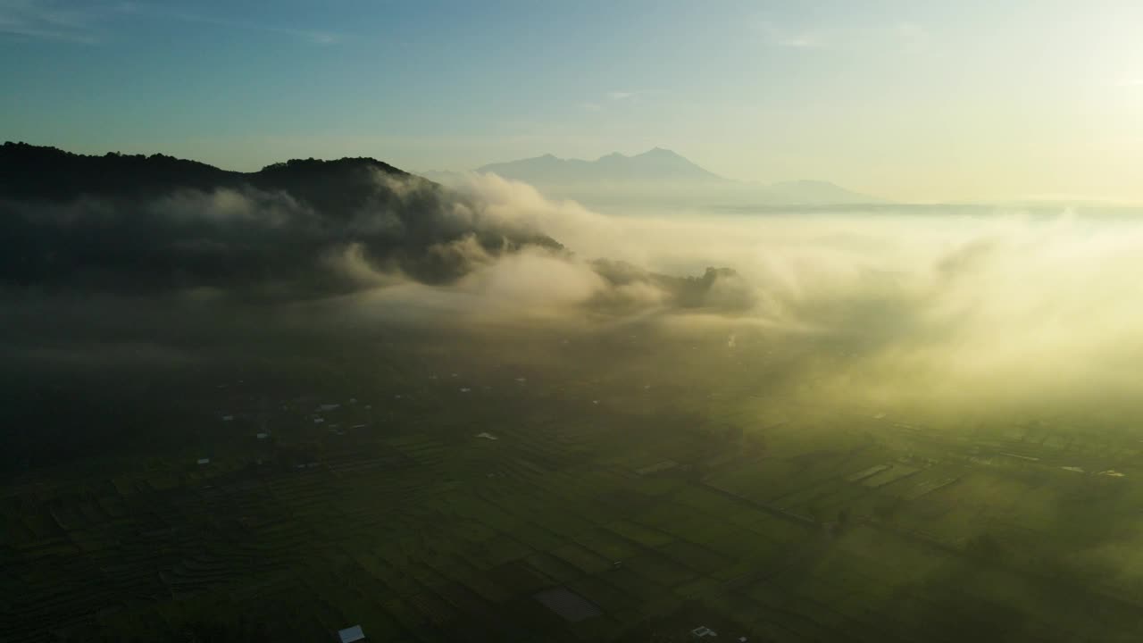 鸟瞰图，从大雾笼罩的稻田和村庄上空飞过，可以看到林贾尼山的景色视频素材