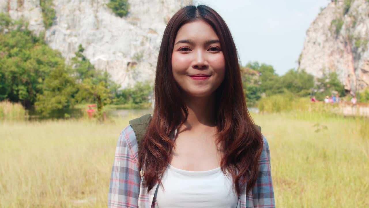 开朗的年轻旅行家与背包感觉快乐的亚洲女士微笑相机在山湖。视频素材