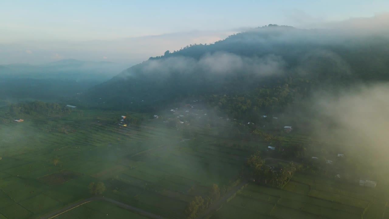 鸟瞰图，一个村庄的稻田和山丘在早晨笼罩在薄雾中视频素材