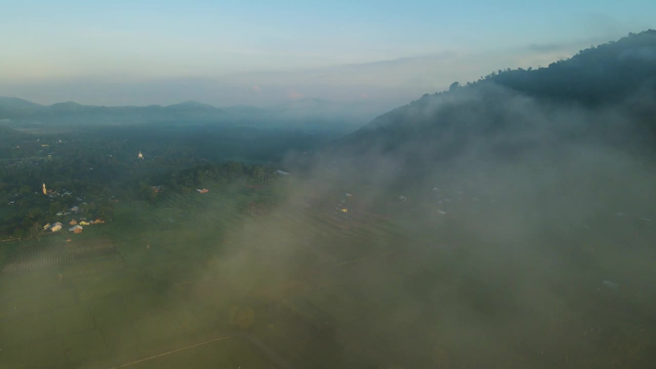 鸟瞰图，一个村庄的稻田和山丘在早晨笼罩在薄雾中视频素材