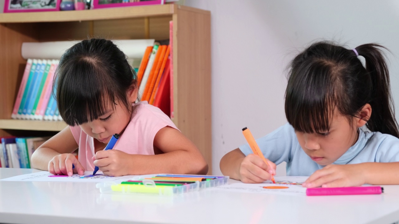 小女孩和她的朋友坐在教室里涂色。两个小妹妹在家上学。小学生喜欢一起学习。回到学校视频素材