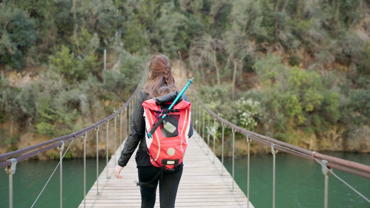 一个徒步旅行的女人走过一座吊桥。视频素材