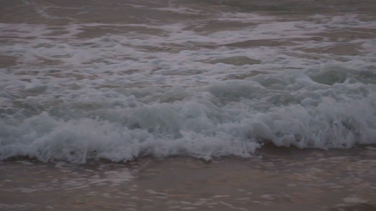 在印度果阿的巴加海滩上的泡沫海浪的特写慢动作。太阳落山后，泡沫汹涌的海浪冲击着海滩。自然波背景。视频素材