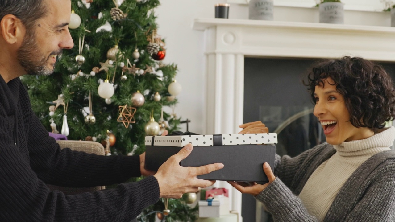 丈夫在客厅的圣诞树旁给妻子送圣诞礼物视频素材
