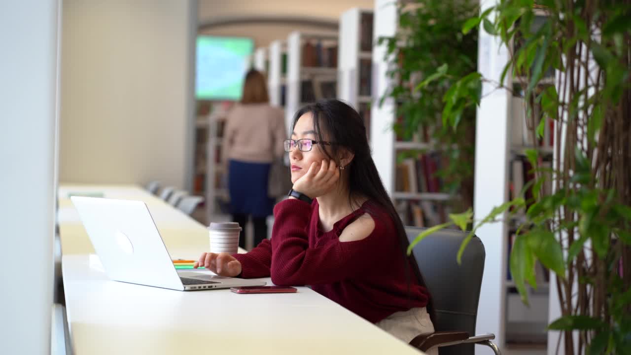 年轻的亚洲学生女孩在大学图书馆学习与笔记本电脑准备考试做研究视频素材