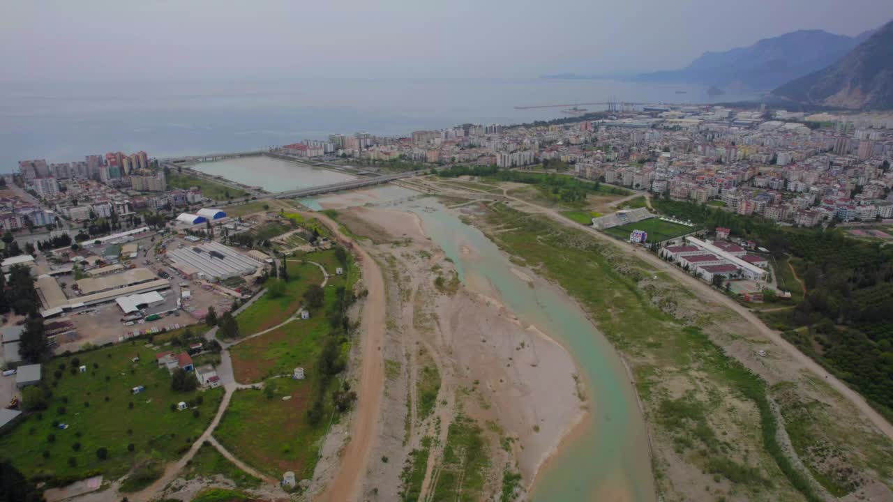 用无人机向后飞越河床，俯瞰城市、大海和山脉。视频素材