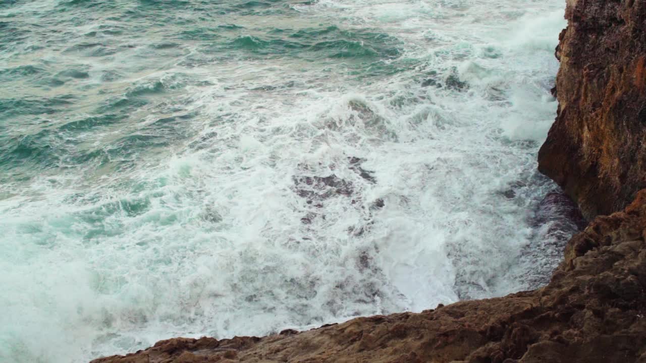 大海冲击岩石海岸，绿色的水溅和创造白色泡沫，从上面看，慢动作视频视频素材