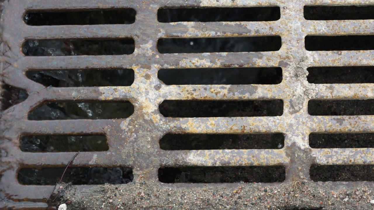 污浊的雨水流向城市街道上生锈的金属排水沟视频素材