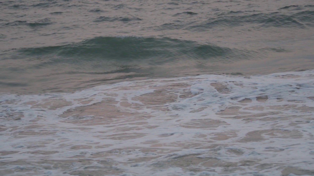 特写在印度果阿的巴嘎海滩上的泡沫海浪的缓慢运动。太阳落山后，冒着泡沫的海浪拍打着海滩。自然波背景。视频素材