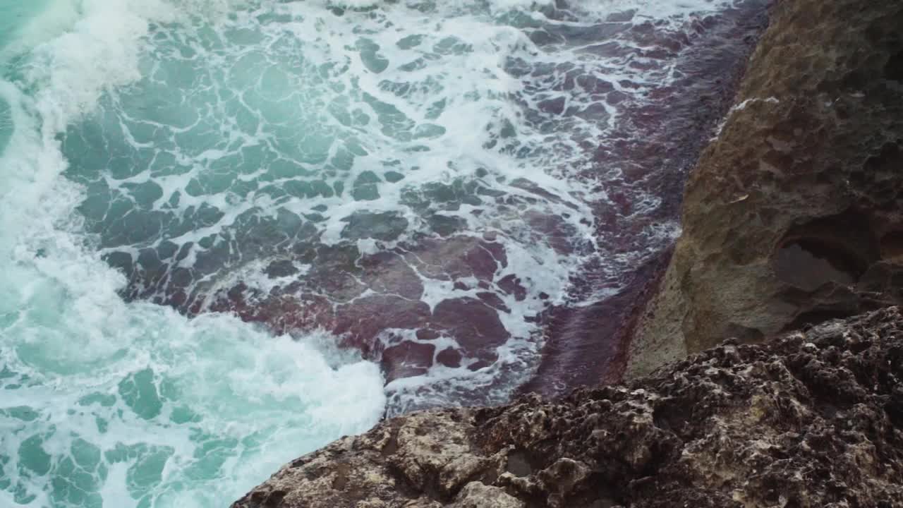 大海冲击岩石海岸，绿色的水溅和创造白色泡沫，从上面看，慢动作视频视频素材