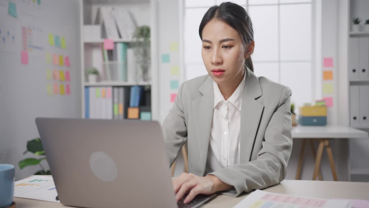 年轻的亚洲女商人坐在桌子上，因过度工作压力而疯狂，愤怒的大量工作在办公室尖叫。视频素材