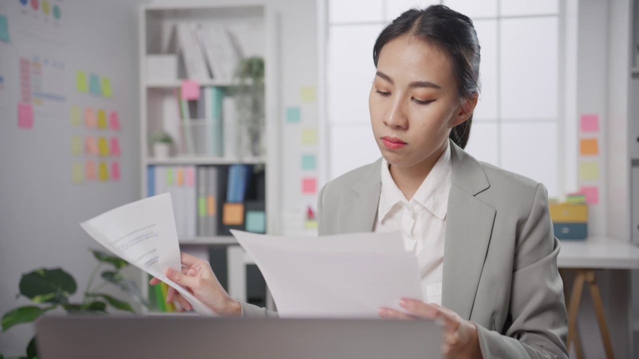 年轻的亚洲女商人坐在办公桌上生气的与财务报告问题撕文件纸在办公室。视频素材