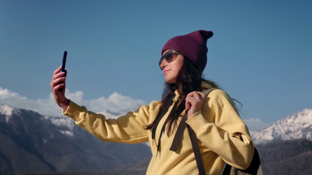 微笑背包旅行的女人摆姿势自拍智能手机在山雪峰天空景观视频素材