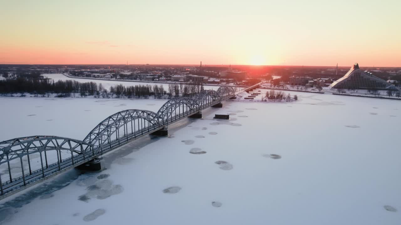 无人机俯瞰里加的铁路桥，冰冻的道格瓦河，日落时被雪覆盖的树木，拉脱维亚，欧洲视频素材