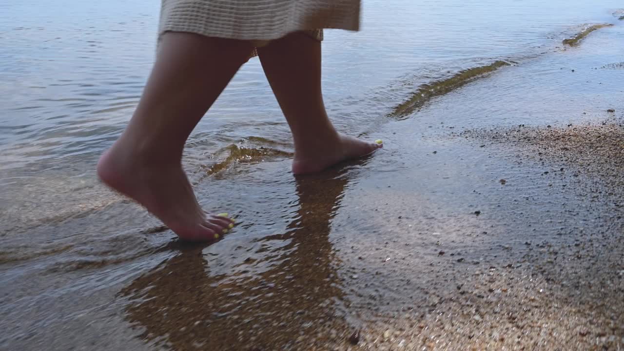 女人的腿踏着海浪走在沙滩上。视频素材