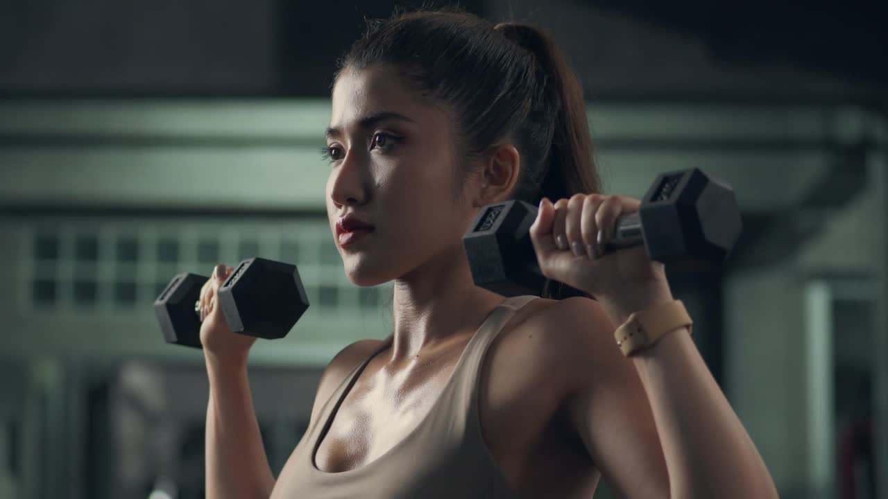 一位穿着内衣和打底裤的年轻亚洲女性在健身房举哑铃视频素材