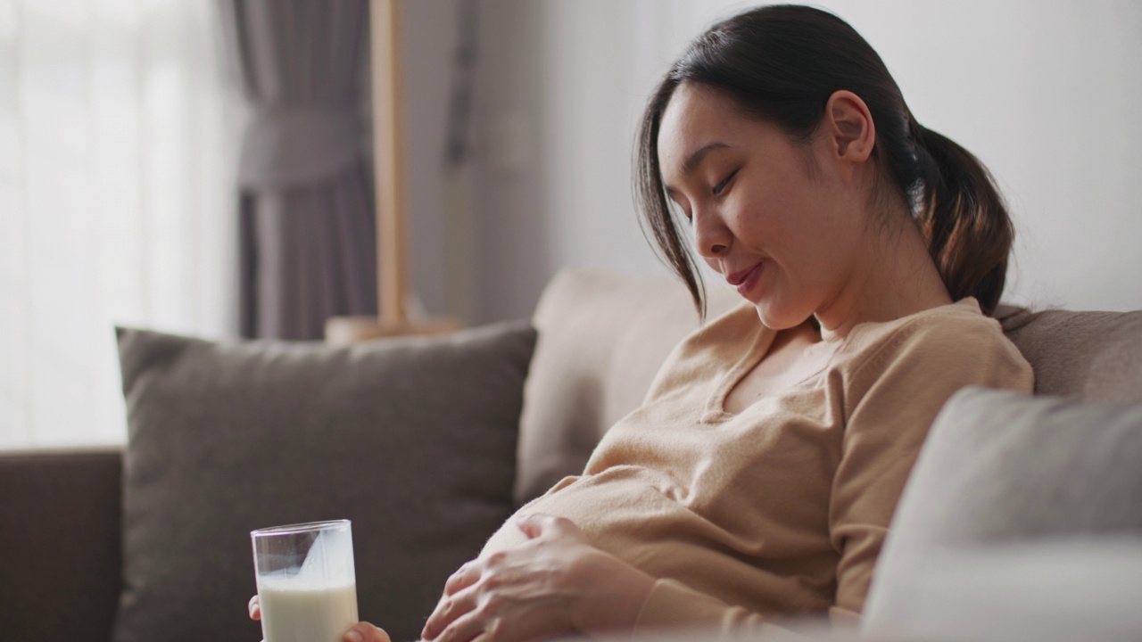 孕妇喝着牛奶，轻轻摸着肚子视频素材