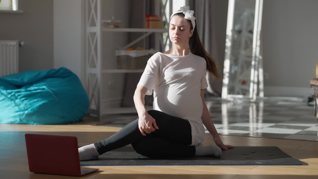 广角肖像自信怀孕年轻女子坐在锻炼垫子上观看在线健身课笔记本电脑。身材苗条的白人准妈妈在家做运动。运动和女性气质。视频素材