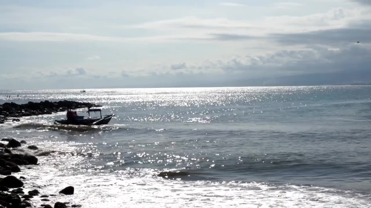 阳光反射在海水上的美丽海滩景色，看着渔船经过视频素材