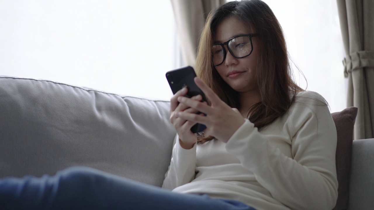 年轻女子在家里的客厅里放松，使用手机视频素材