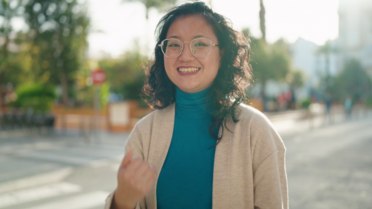 年轻的中国女子微笑着自信地在街上用手指做着手势视频素材