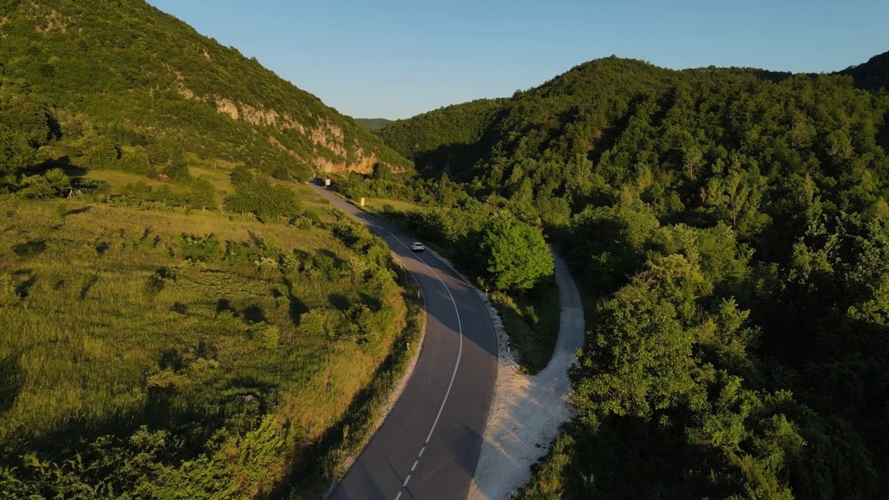 在道路上的俯视图无人机跟随汽车，而驾驶旅游和旅游交通概念，在春天或夏天的一天，通过田野和树木在阳光下的日落塞尔维亚Knjazevac视频素材