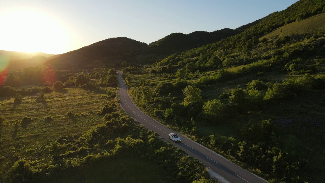 在道路上的俯视图无人机跟随汽车，而驾驶旅游和旅游交通概念，在春天或夏天的一天，通过田野和树木在阳光下的日落塞尔维亚Knjazevac视频素材