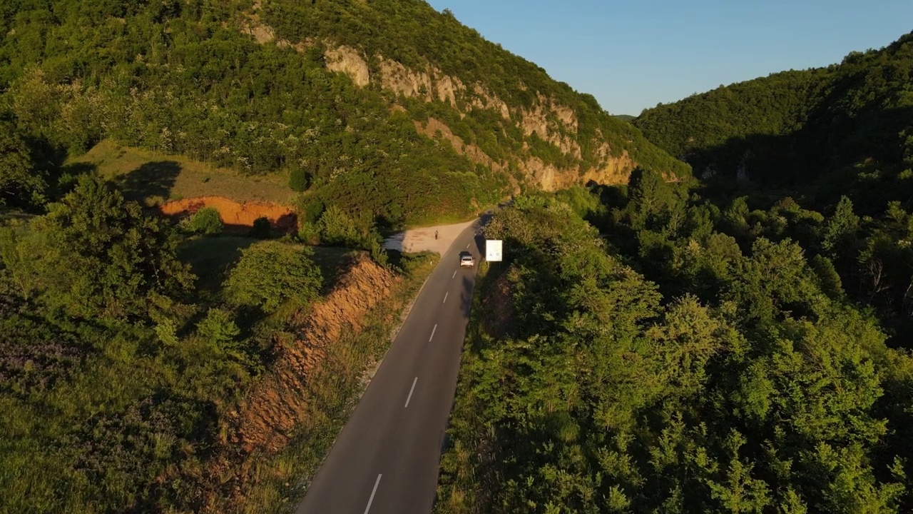 在道路上的俯视图无人机跟随汽车，而驾驶旅游和旅游交通概念，在春天或夏天的一天，通过田野和树木在阳光下的日落塞尔维亚Knjazevac视频素材