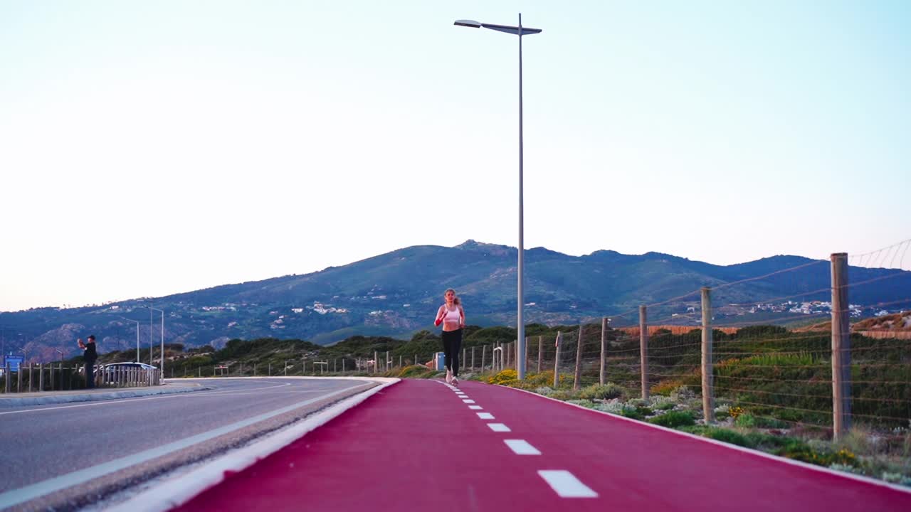 全长视图运动女性慢跑者跑步自行车道附近的道路与山的背景。运动型女子慢跑自然。健康的生活方式视频素材