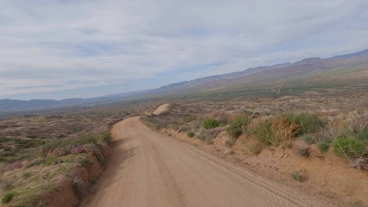 在远处群山环绕的沙漠中行驶在一条尘土和砾石的道路上。视频下载