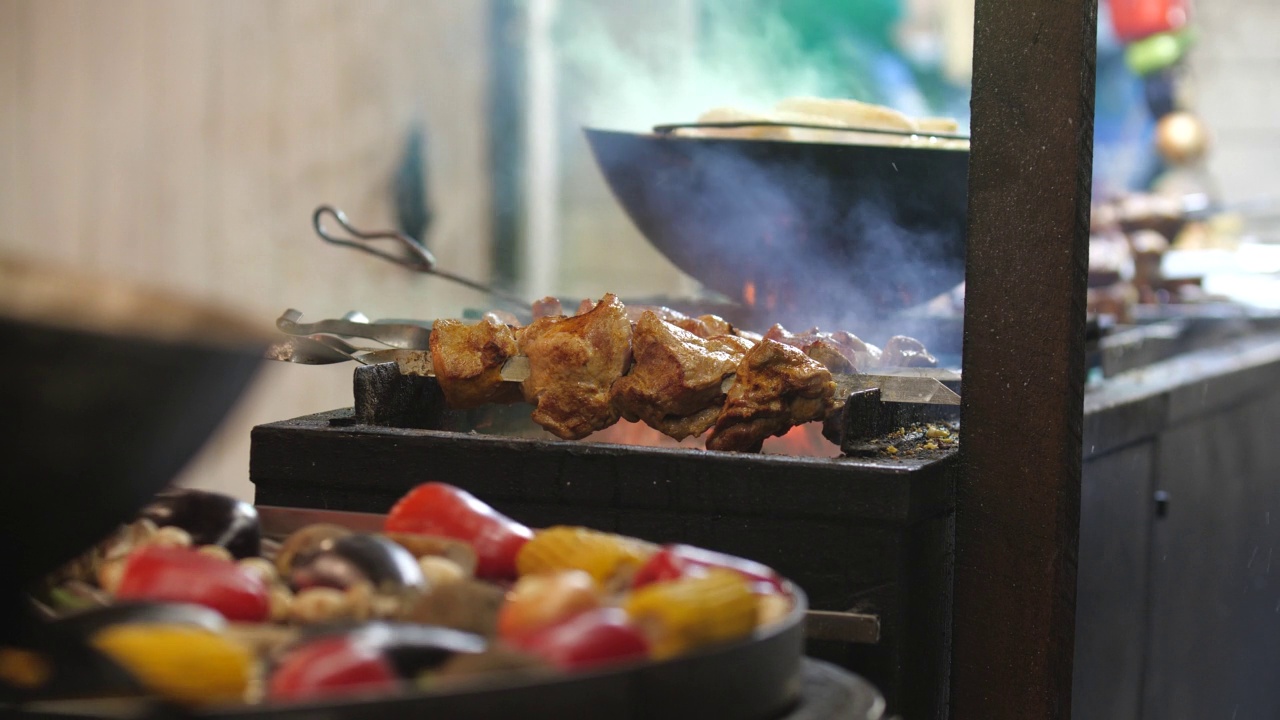 烹饪街头食物的特写镜头。多汁的肉串和蔬菜在烤架上的炭火上炸。野餐或晚上烧烤。冬季集市，户外贸易。视频素材