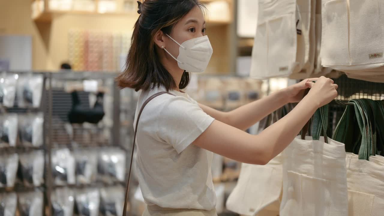 快乐微笑的女人选择新的休闲服装衣服在最小的商店购物她快乐放松在商店前戴着口罩保护视频素材