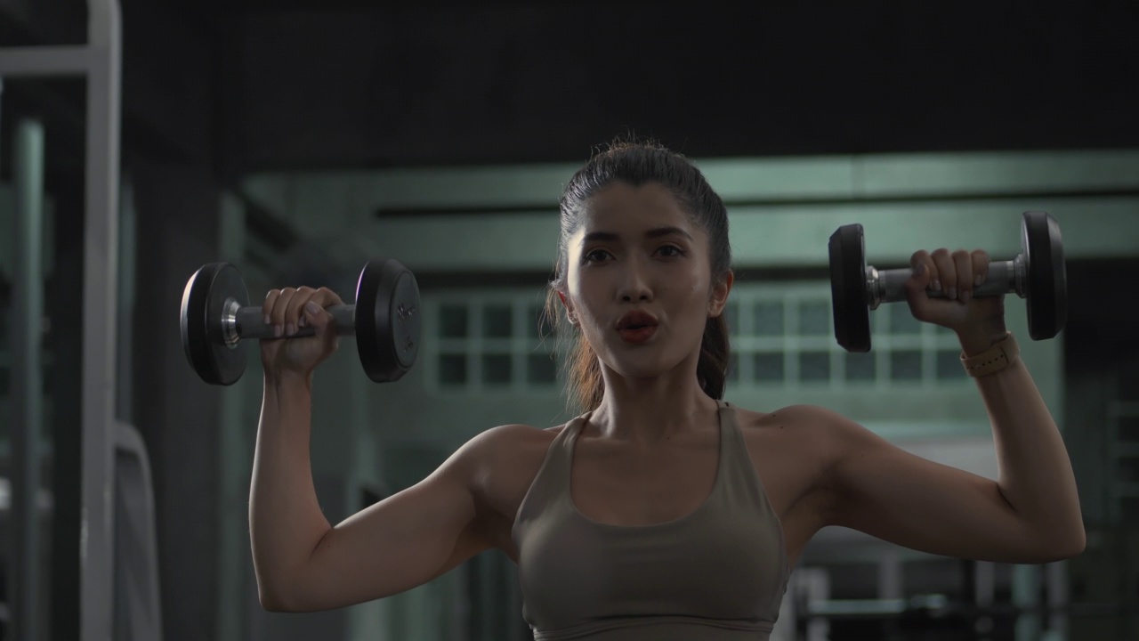 一位穿着胸罩和紧身裤的年轻亚洲女性正在健身房举哑铃视频素材