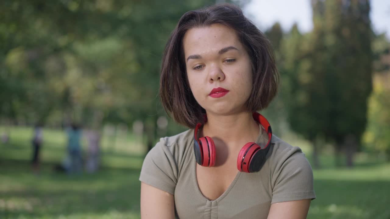 年轻的白人女性侏儒症手势心形伸展手看着镜头。前视图肖像小人摆慢动作休息在春夏公园户外。视频素材