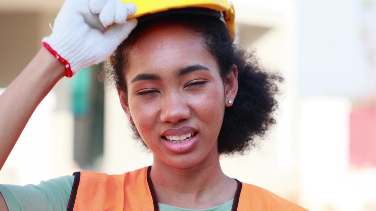 特写黑人女性的脸。图为在建筑工地上戴着黄色安全帽的非洲裔美国女工程师。视频素材