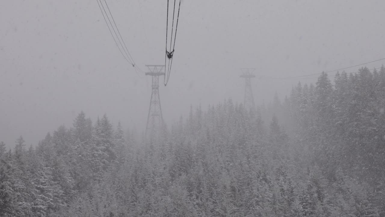 鸟瞰缆车塔，俯瞰白雪覆盖的常青树和岩石峭壁视频素材