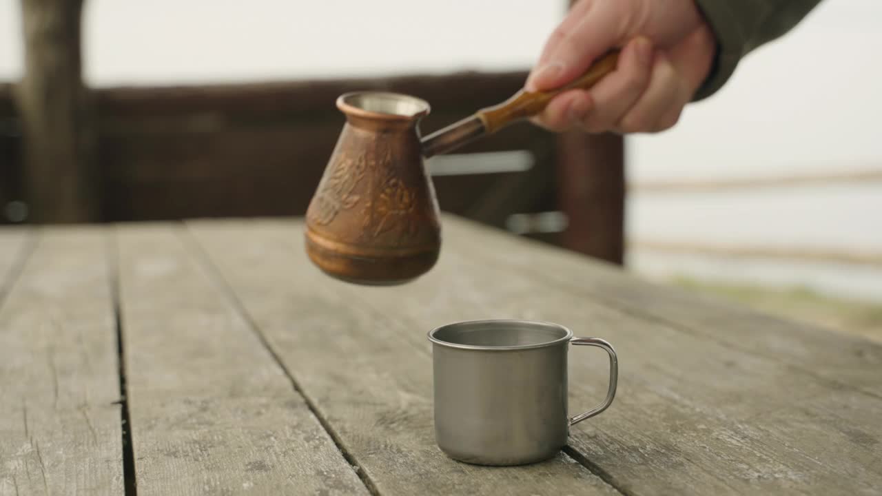 咖啡被倒进一个用铜杯子做成的金属杯里。户外休闲的概念。视频素材