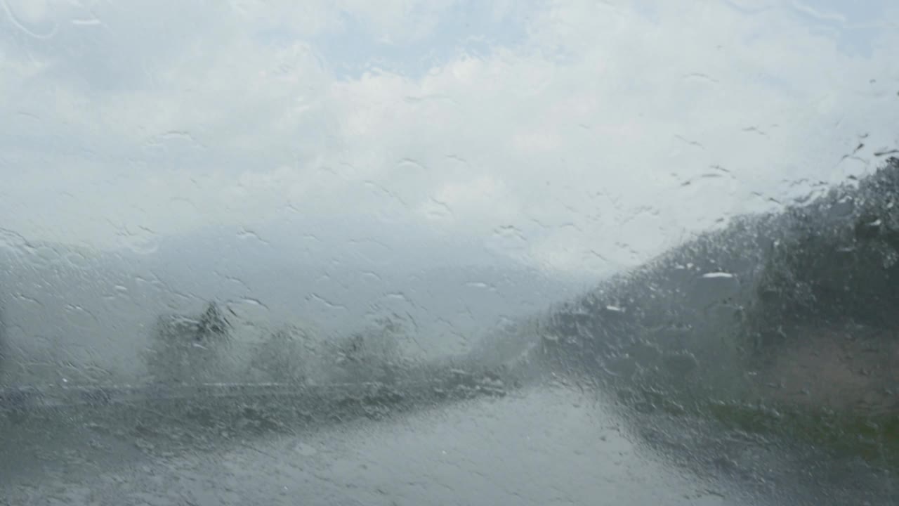 一辆在山路上行驶的汽车被倾盆大雨灌满了玻璃。雨刷可以清除挡风玻璃上的积水。由于能见度低，倾盆大雨对交通构成危险视频素材