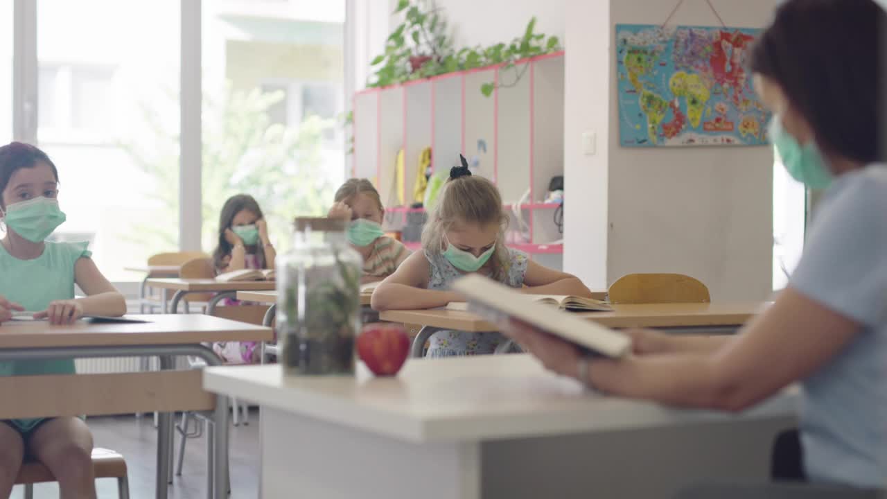 孩子们在学校的教室里戴着面具坐在教室里听老师讲课。大流行期间在学校的课程。视频素材