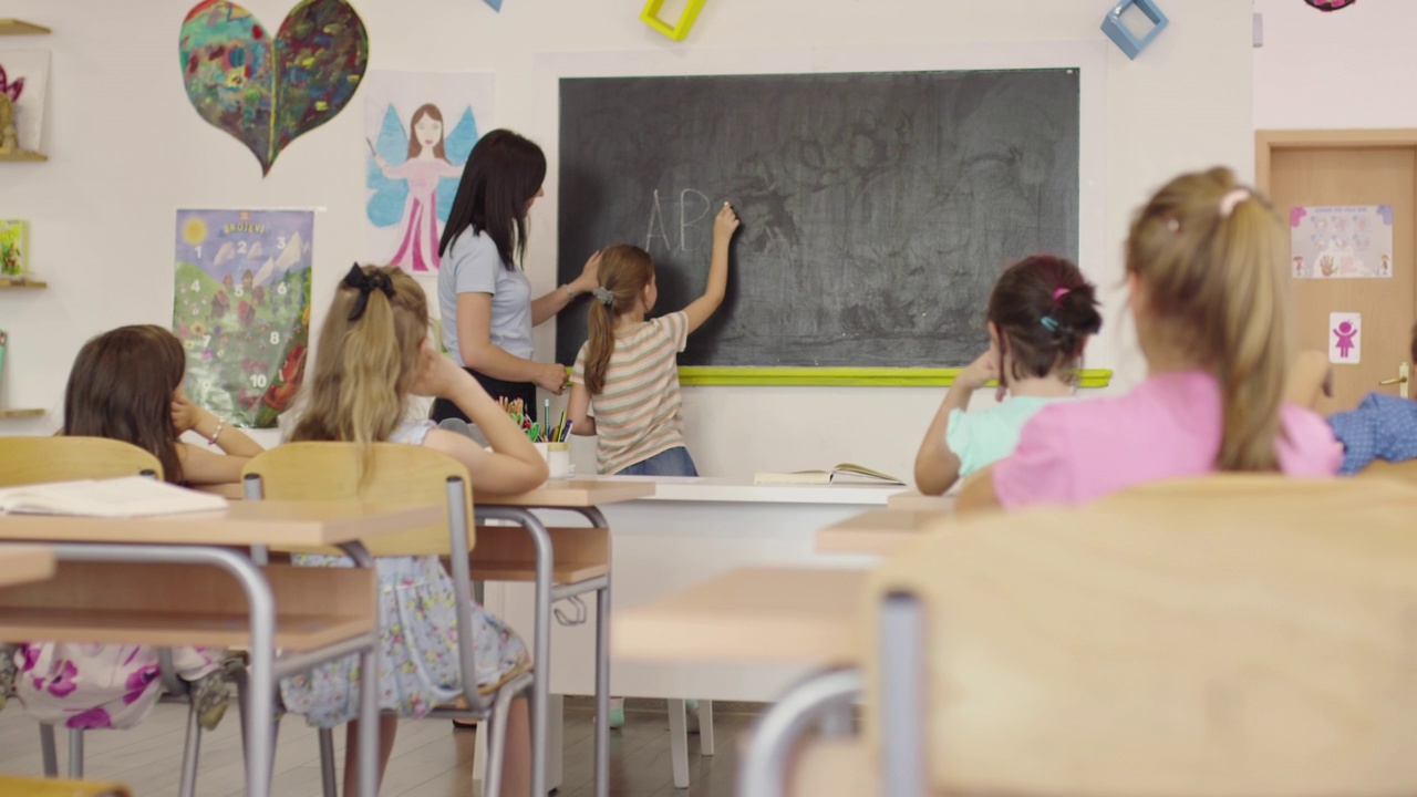 小学。女老师一边帮助学生一边把答案写在黑板上。视频素材