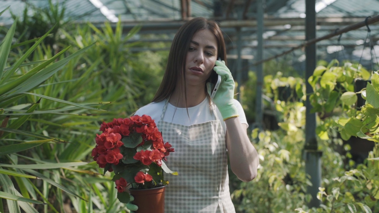 一个手持鲜花的小女孩在花房里讲着电话，背景是植物。慢动作视频素材