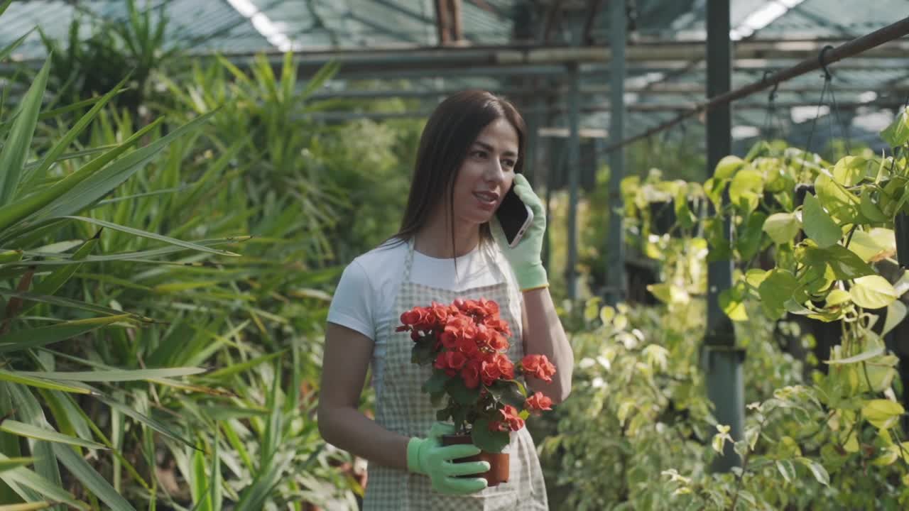 一个手持鲜花的小女孩在花房里讲着电话，背景是植物。慢动作视频素材