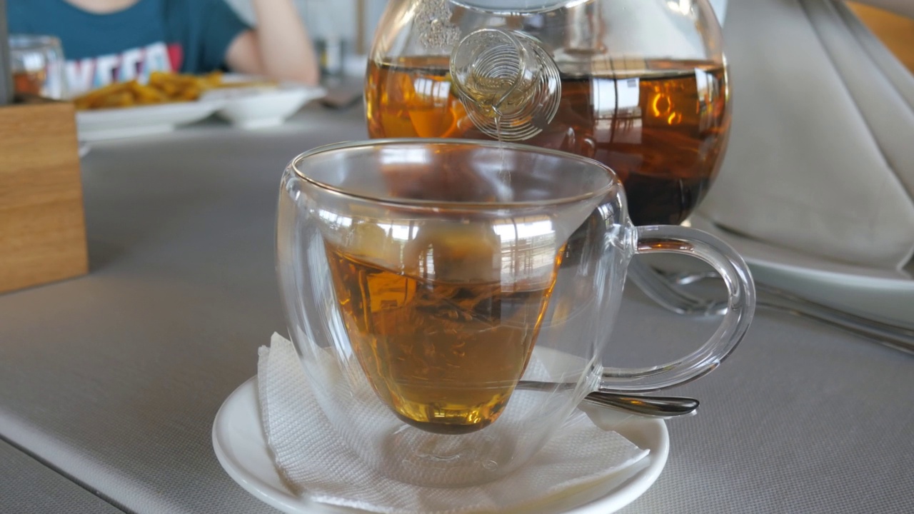 透明杯架，然后将热锡兰茶从玻璃茶壶倒入杯中。餐厅服务员。视频下载