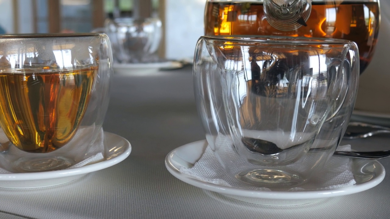 透明杯架，然后将热锡兰茶从玻璃茶壶倒入杯中。餐厅服务员。两杯红茶。视频下载