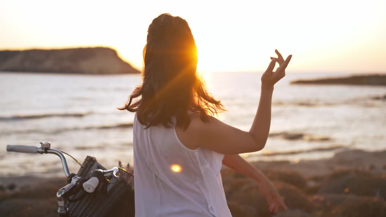 背影苗条美丽的女人在阳光下跳舞在慢动作微笑休息在日落塞浦路斯。愉快愉快轻松的白人游客戴着耳机听着音乐享受假期。视频素材